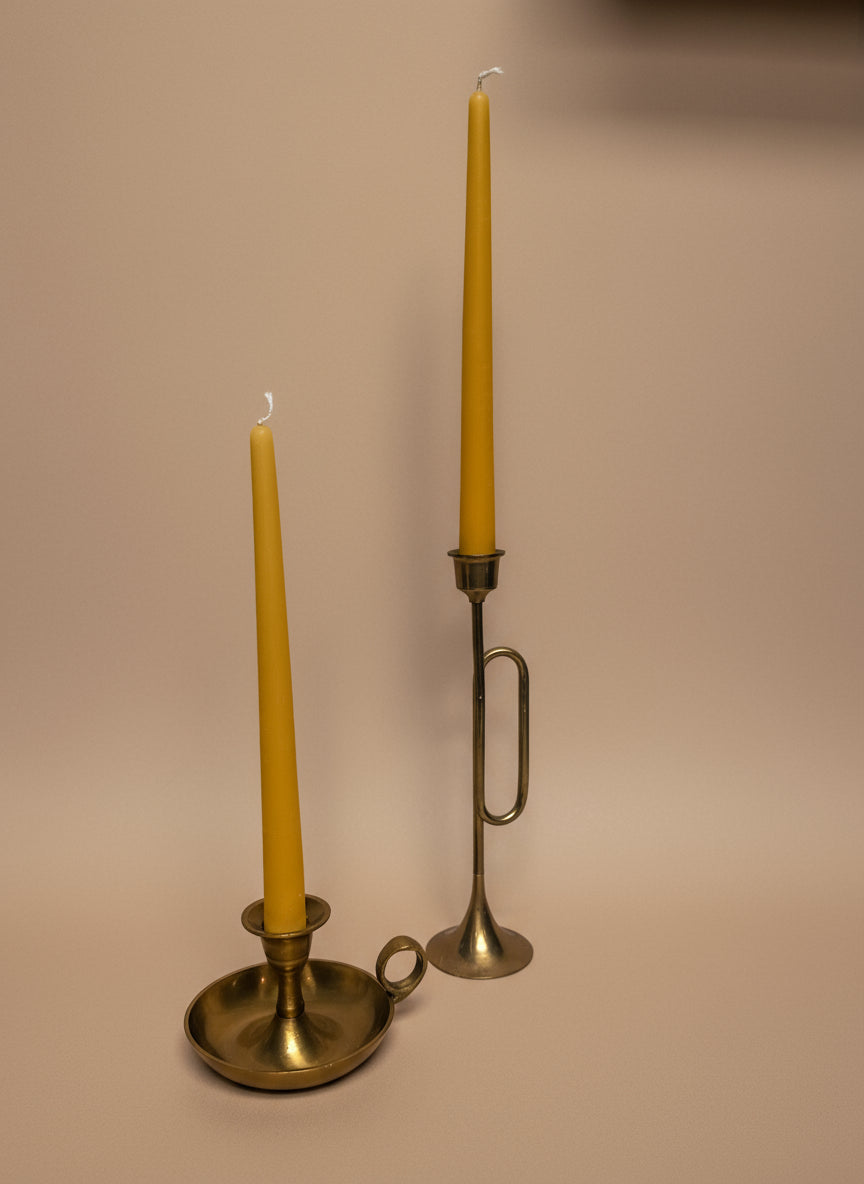 Two brass candle holders with yellow beeswax taper candles on a warm background