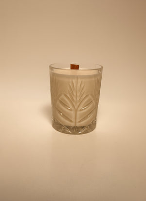 Candle in a glass container with leaf design on a beige background