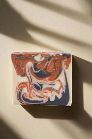 Marbled soap bar with orange, white, and black swirls on a white background