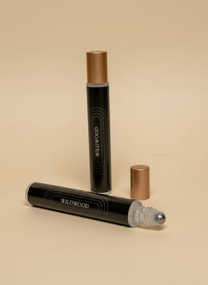 Two black rollerball bottles with gold caps on a tan background