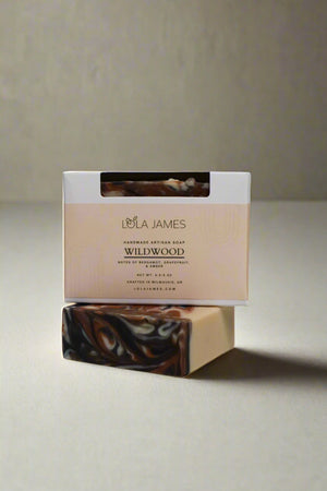 Lola James Wildwood soap bar with packaging on a white background. Soap is white with black and orange swirl pattern.