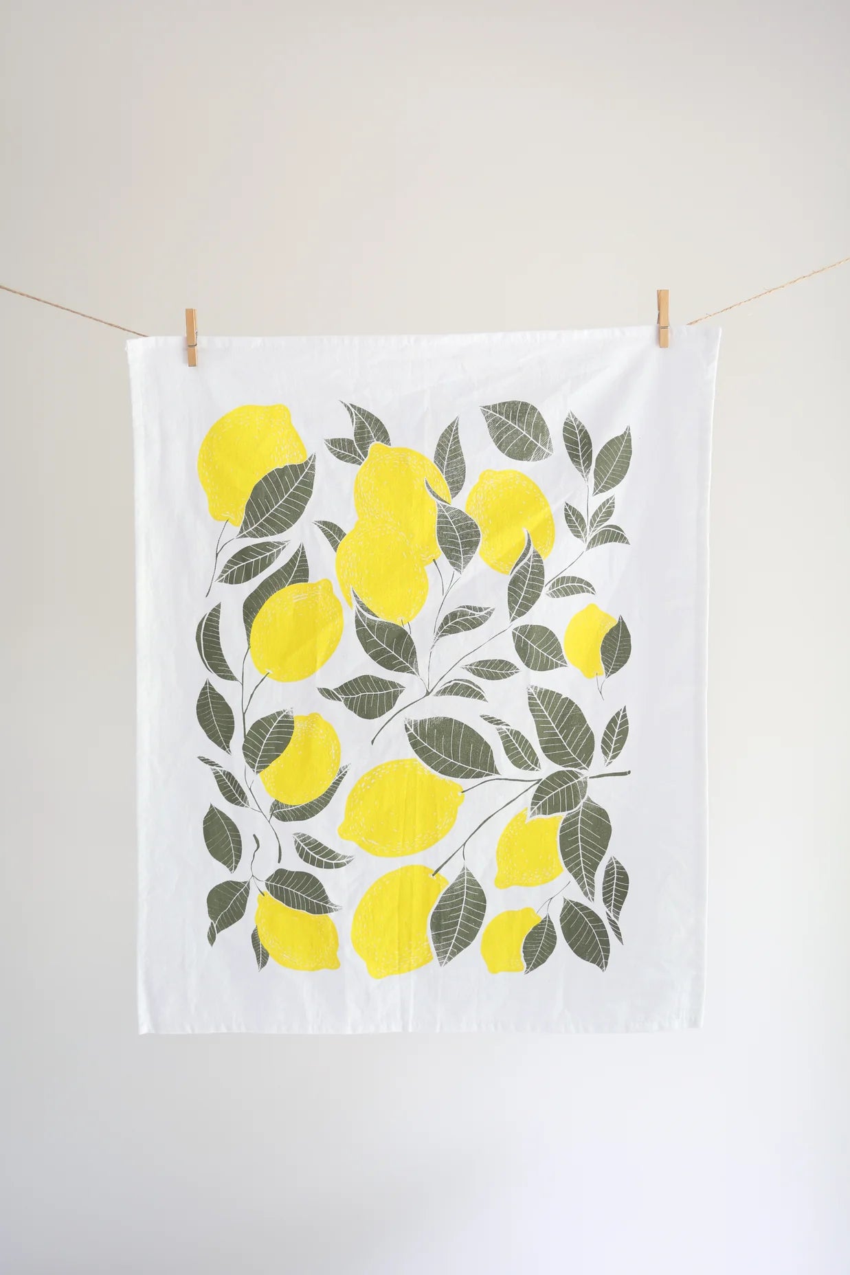 Tea towel with lemon design hanging on a line against a white wall