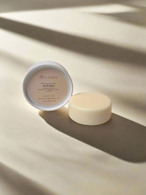 White and cream packaging next to a body butter bar with neutral background.
