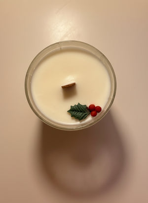 Candle with decorative holly elements on a plain background