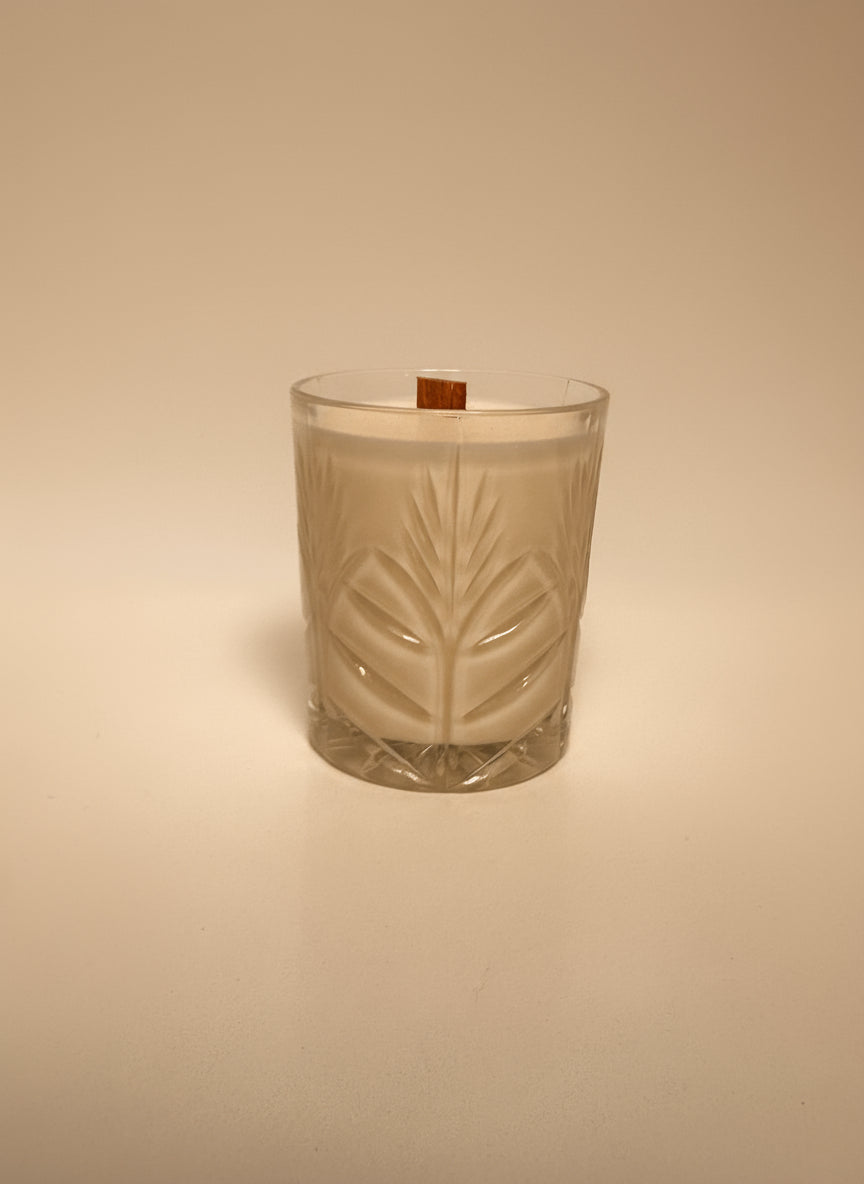 Candle in a glass container with leaf design on a beige background