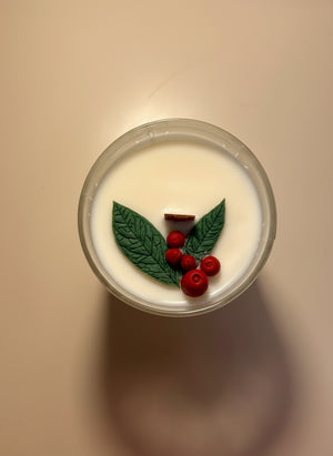 Candle with berry and leaf embeds and wooden wick on neutral background.
