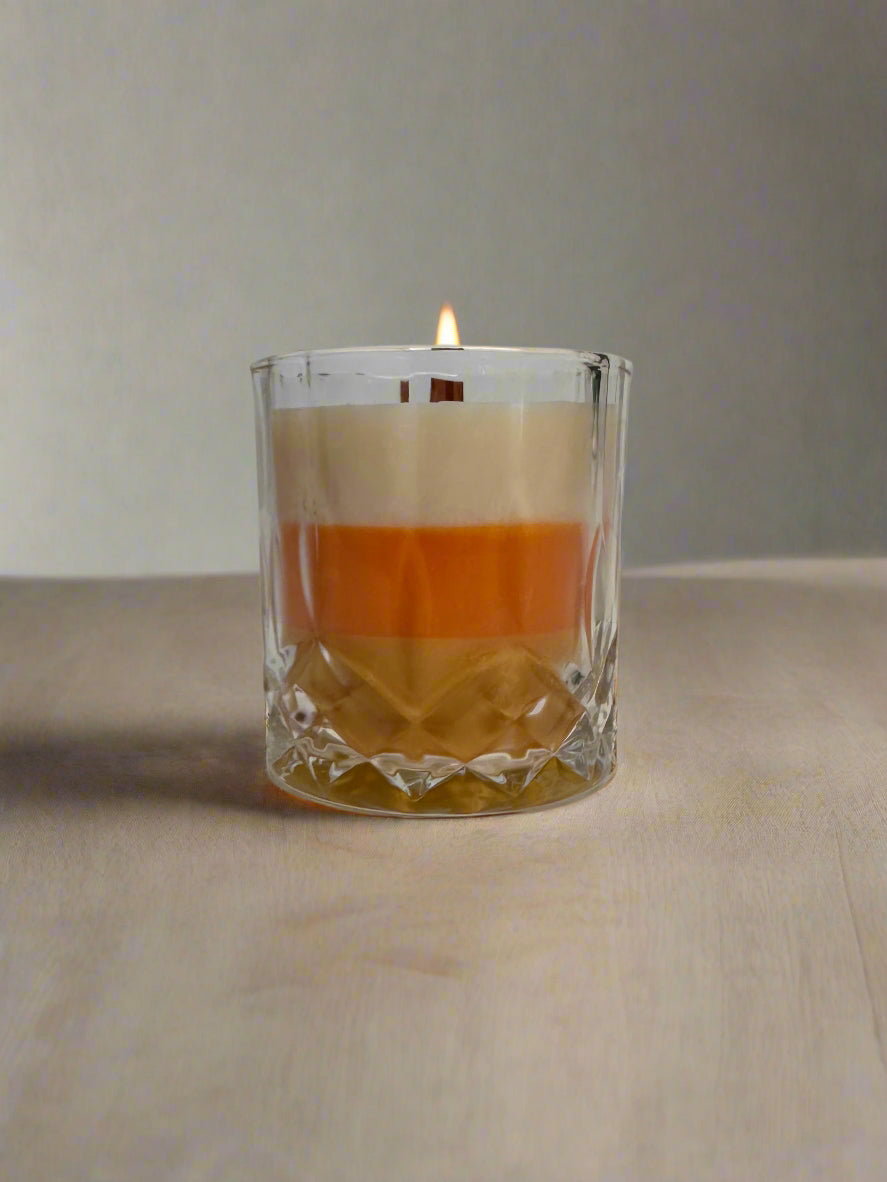 Clear glass candle with candy corn design. Layers of yellow, orange, and white with neutral background.