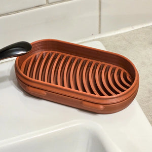 Terracotta soap dish on a bathroom counter with tiled wall in the background