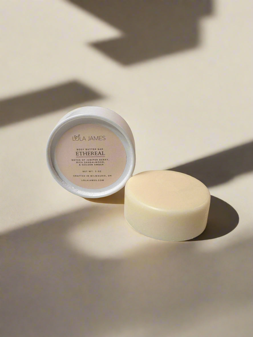 White and cream packaging sitting next to a white body butter bar with neutral background.