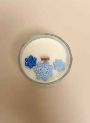 Candle with snowflake-shaped wax pieces on a plain background