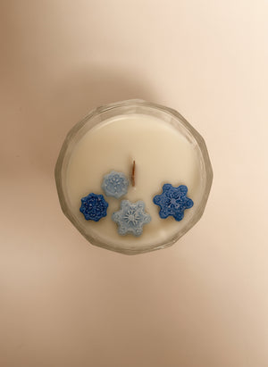 Candle with decorative snowflake-shaped wax pieces on a plain background
