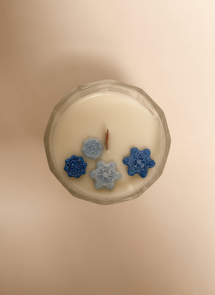Candle with decorative snowflake-shaped wax pieces on a plain background