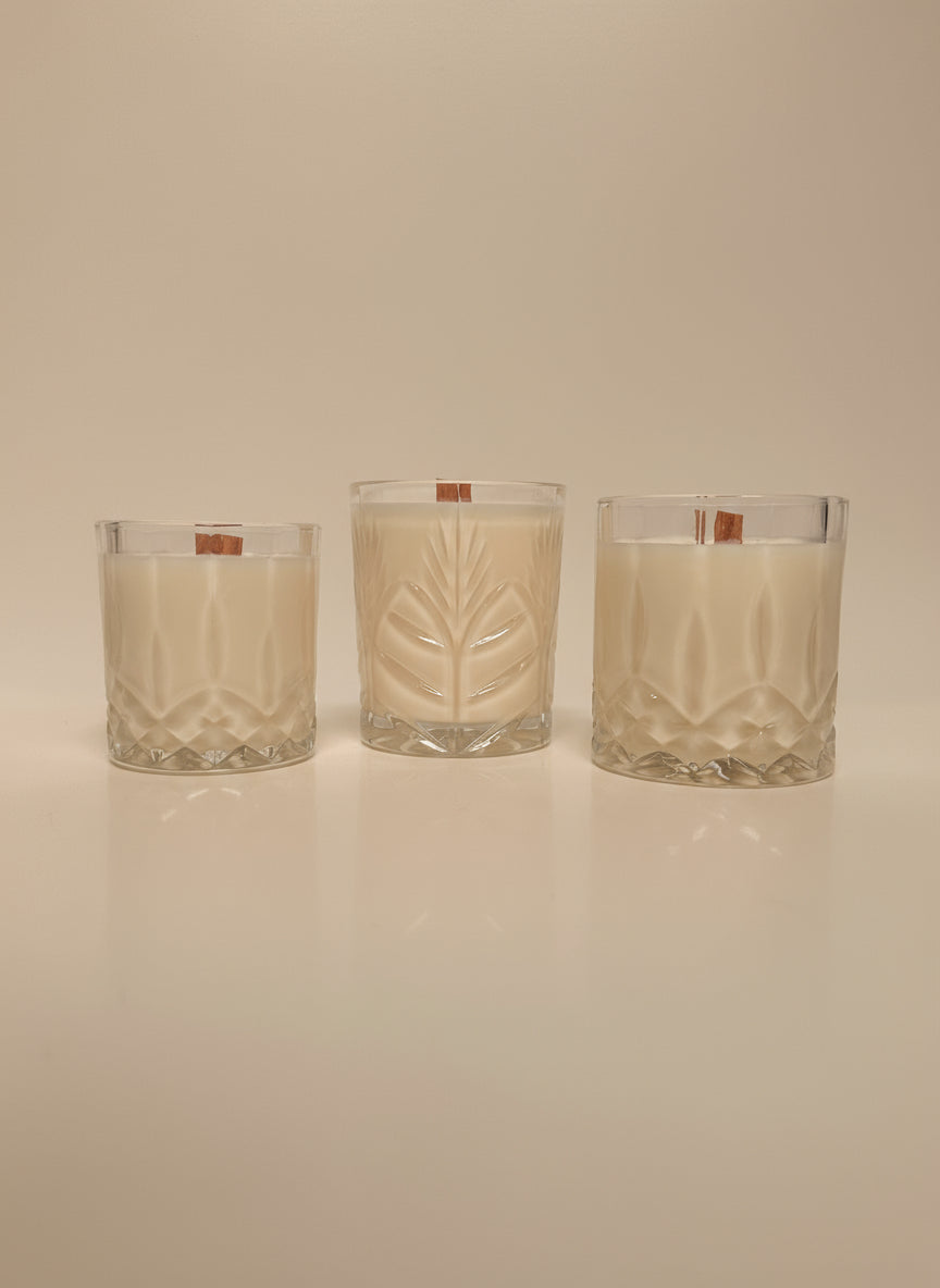 3 clear glass candles with wooden wicks on a cream background. 