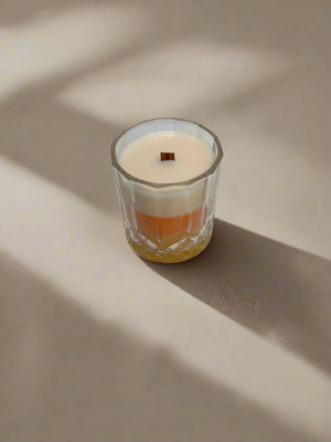 Glass candle with a wooden wick, Candy Corn design with stripes of yellow, orange and white on a gray background