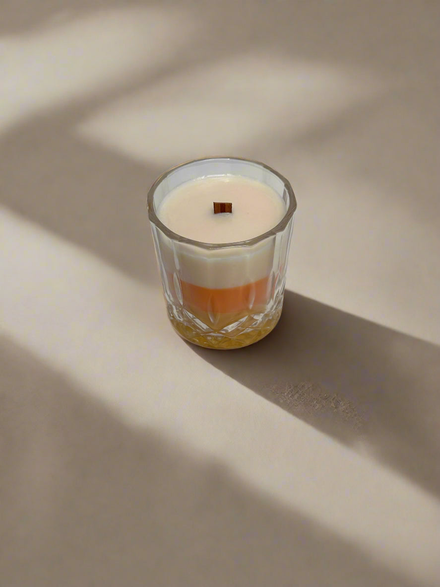 Glass candle with a wooden wick, Candy Corn design with stripes of yellow, orange and white on a gray background