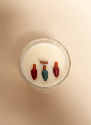 candle with red and green Christmas light embeds on a cream background.