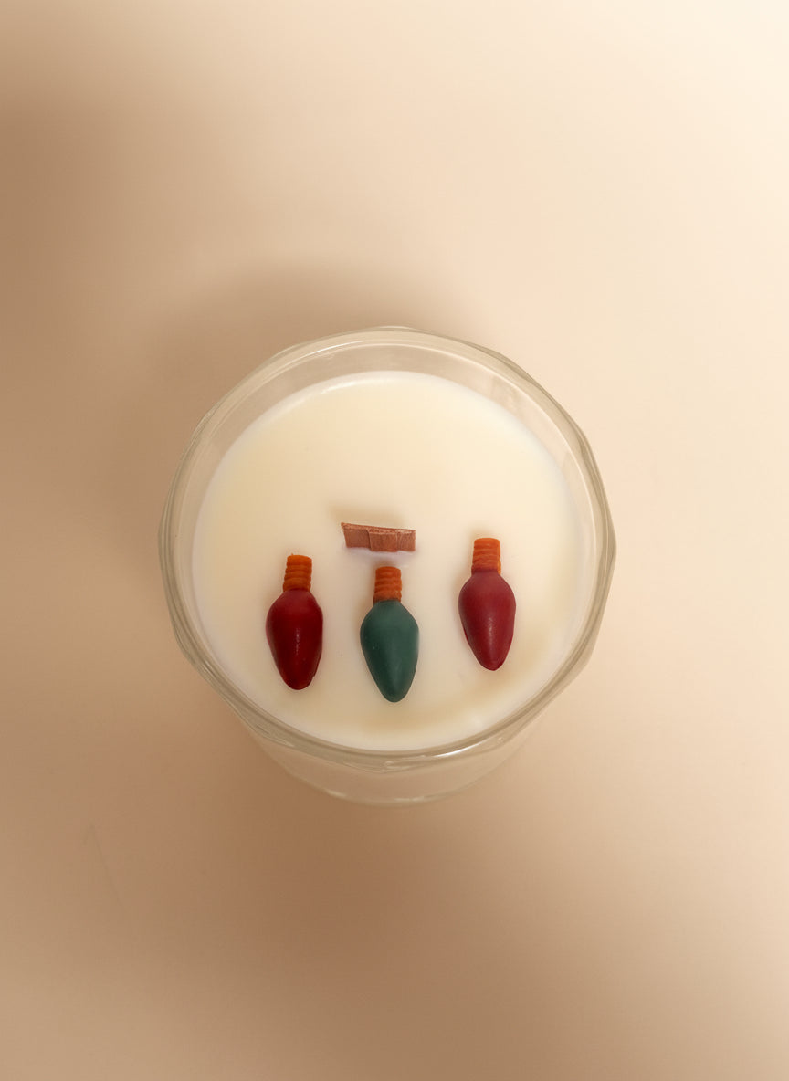 candle with red and green Christmas light embeds on a cream background.