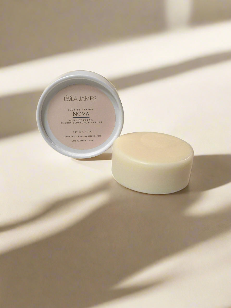 Cream and white packaging sitting next to  a body butter bar with neutral background.