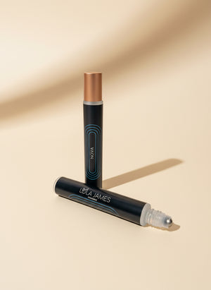 Two fragrance rollerballs with black labels  on a tan background