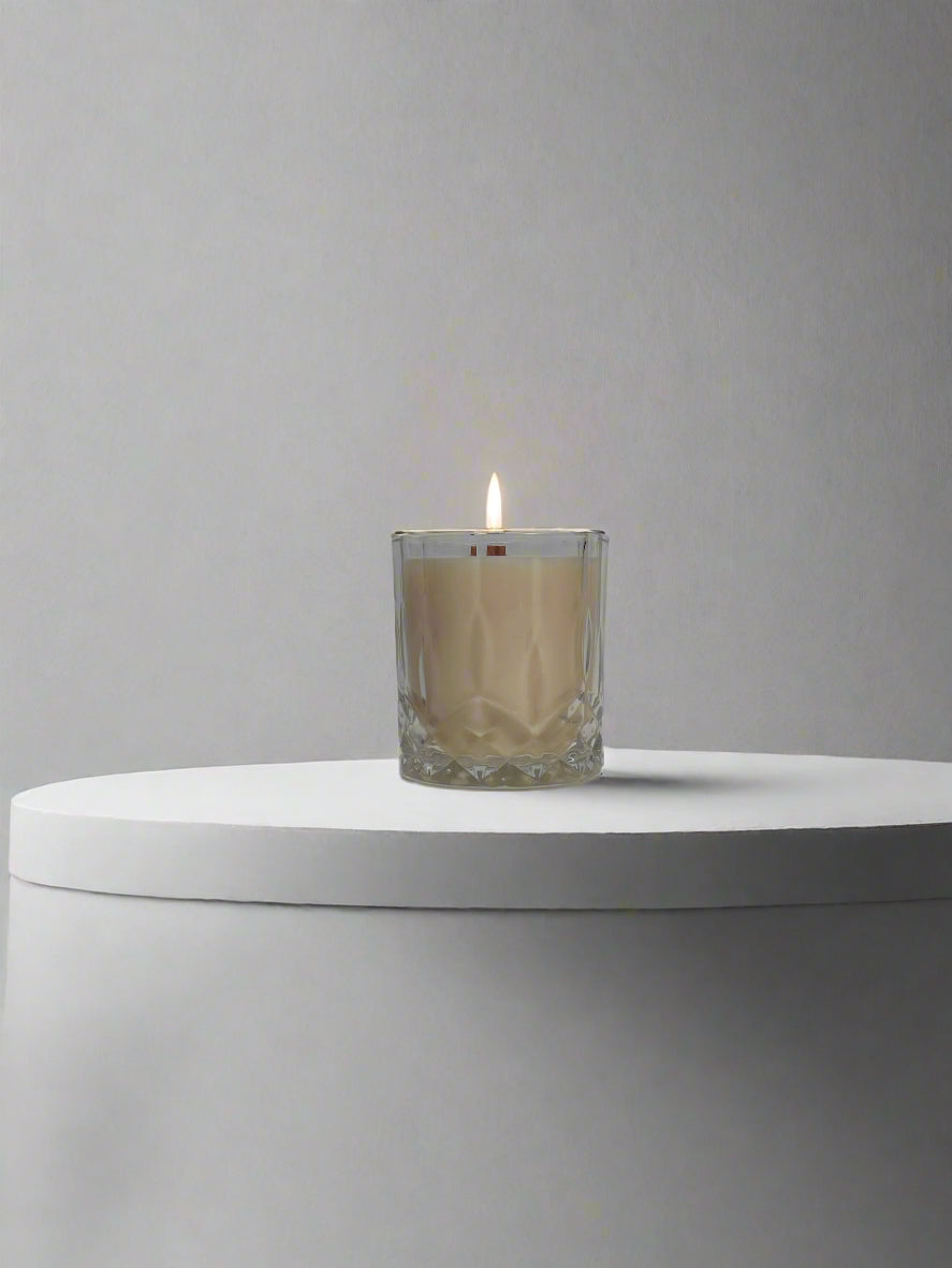 Glass container with soy candle, wooden wick, flame, gray background.