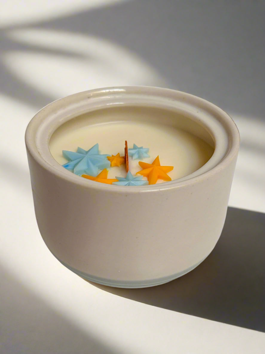 Cream stoneware sugar bowl with blue line on bottom. Yellow and blue star embeds and wooden wick.