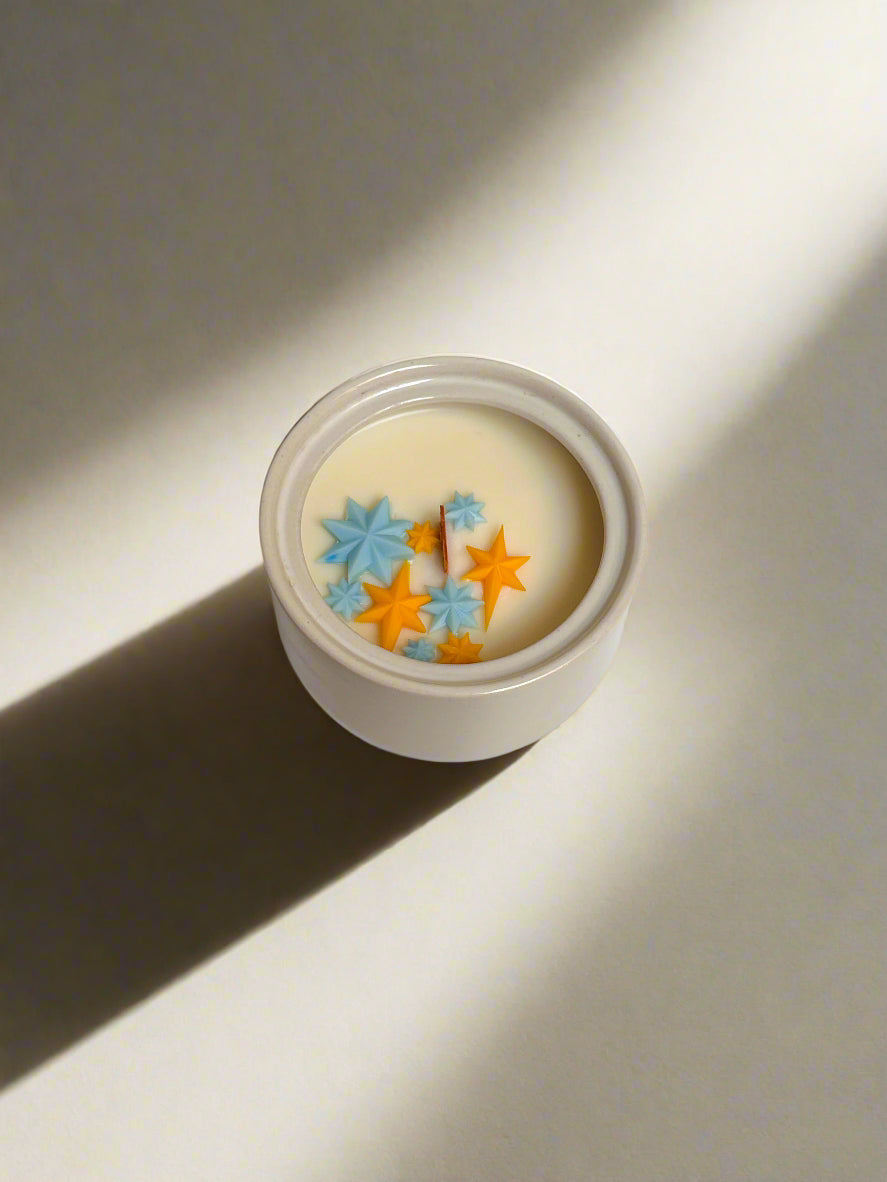 Cream stoneware sugar bowl with blue and yellow star embeds and wooden wick.