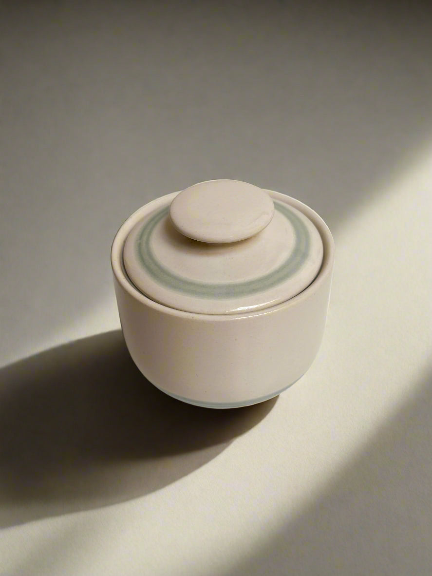 Cream stoneware sugar bowl with lid. Blue line detail.
