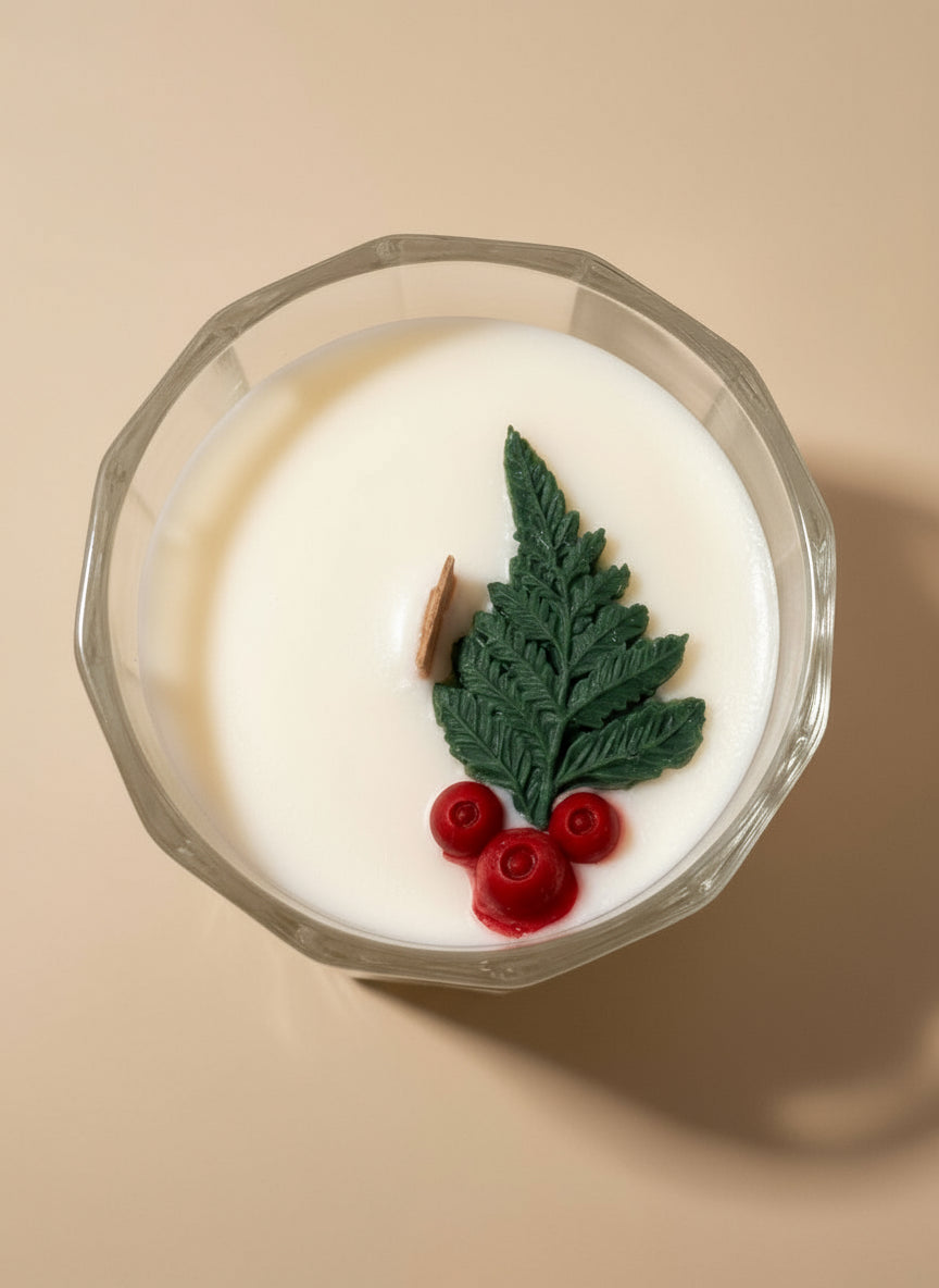 Decorative candle with green leaf and red berries in a glass holder on a white background