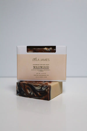 Lola James Wildwood soap bar with packaging on a white background. Soap is white with black and orange swirl pattern.