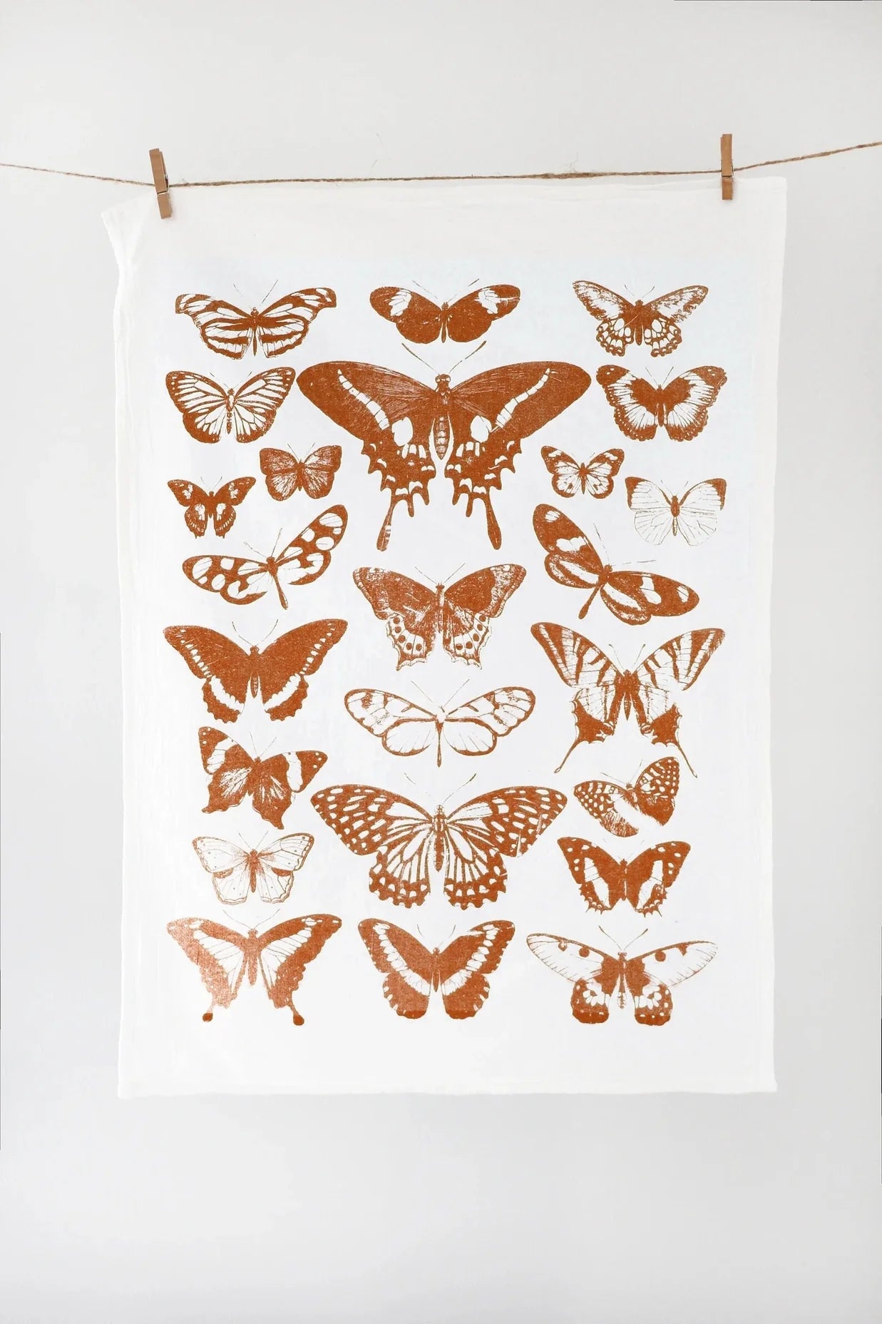 White towel with copper butterfly patterns hanging on a line against a white background