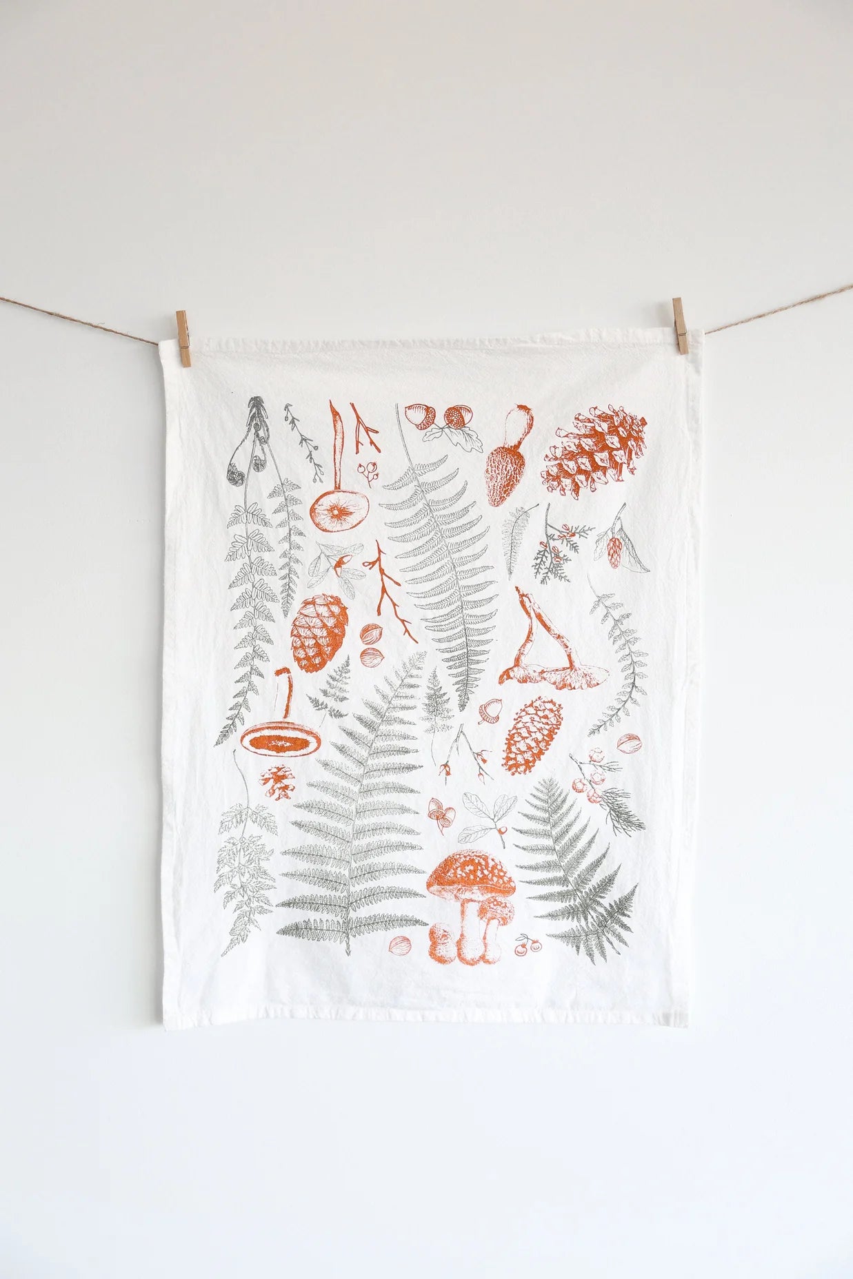 Tea towel with botanical designs hanging on a line against a white background