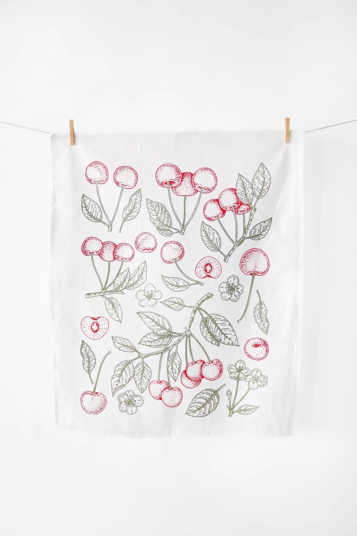 Tea towel with cherry design hanging on a line against a white background